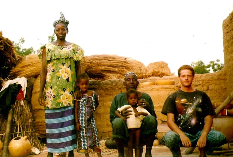 three people and a child pose for a picture in front of a mud hut