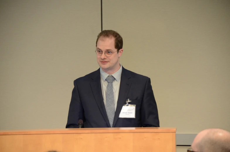 man in suit and tie giving a lecture at podium