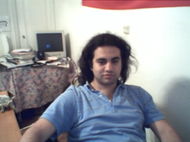 man with long hair sitting down in front of desk