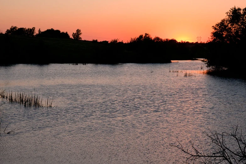 a lake surrounded by trees at sunset time