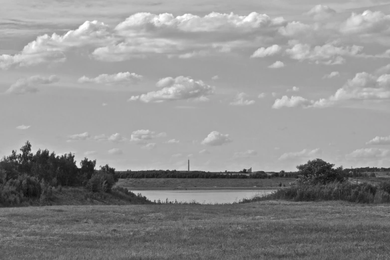 a landscape with green grass, water and clouds in the distance