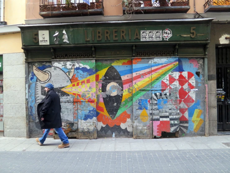 a person walking down the street in front of a building with graffiti on the door