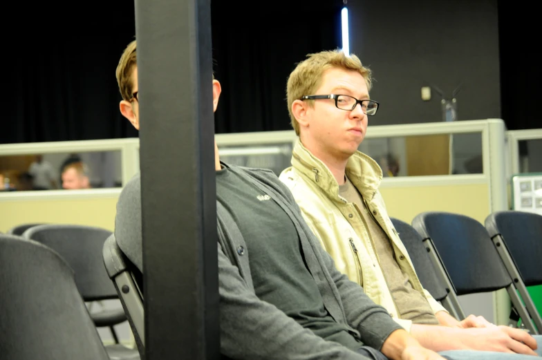 two men are in an auditorium one is wearing glasses