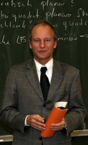 a man holding an orange folder while standing in front of a chalkboard