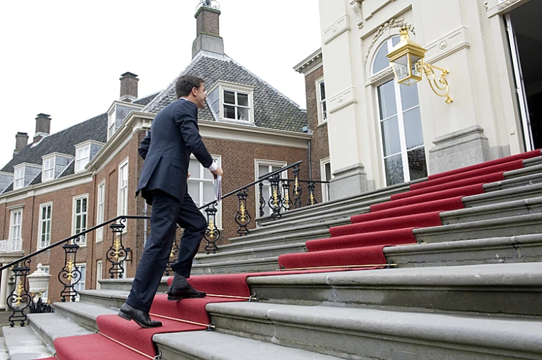 man in black jacket on stair rail with red carpet