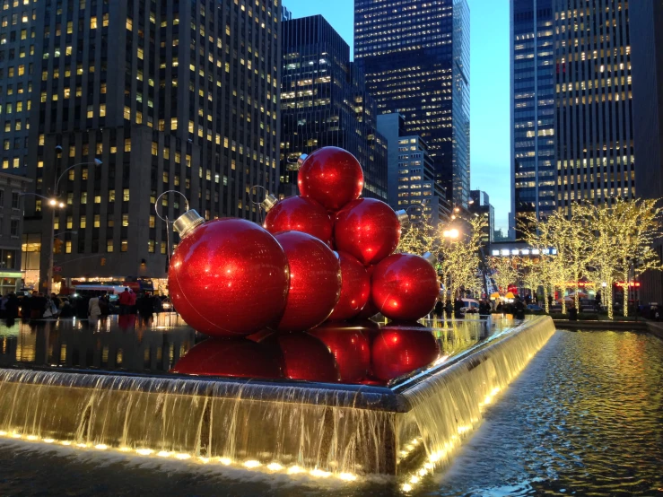 a group of red ornaments standing next to a pond in front of tall buildings