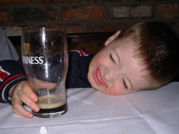 a smiling little boy holding a glass of beer