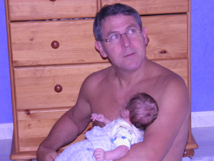 man holding his baby on the chest while in front of a dresser