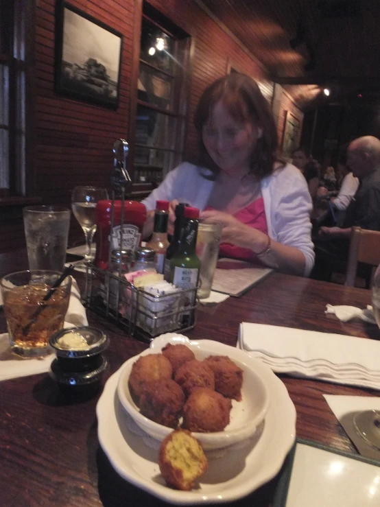 a bowl of food sits on a table near a lady sitting at a table