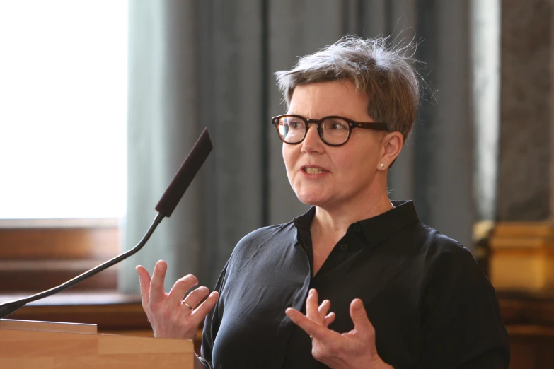 a woman wearing glasses speaking at an audience