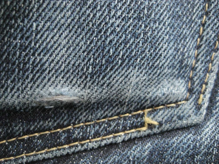a worn and scratched jeans pocket with some yellow stitchs