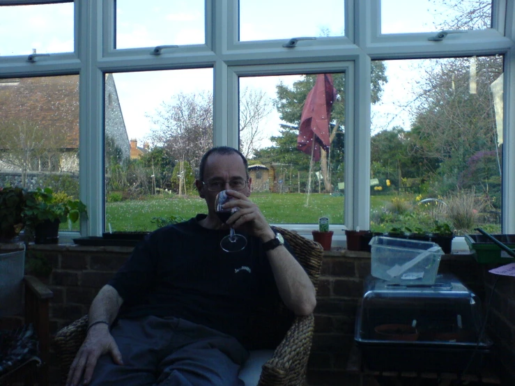 a man drinking from a wine glass in front of a large window