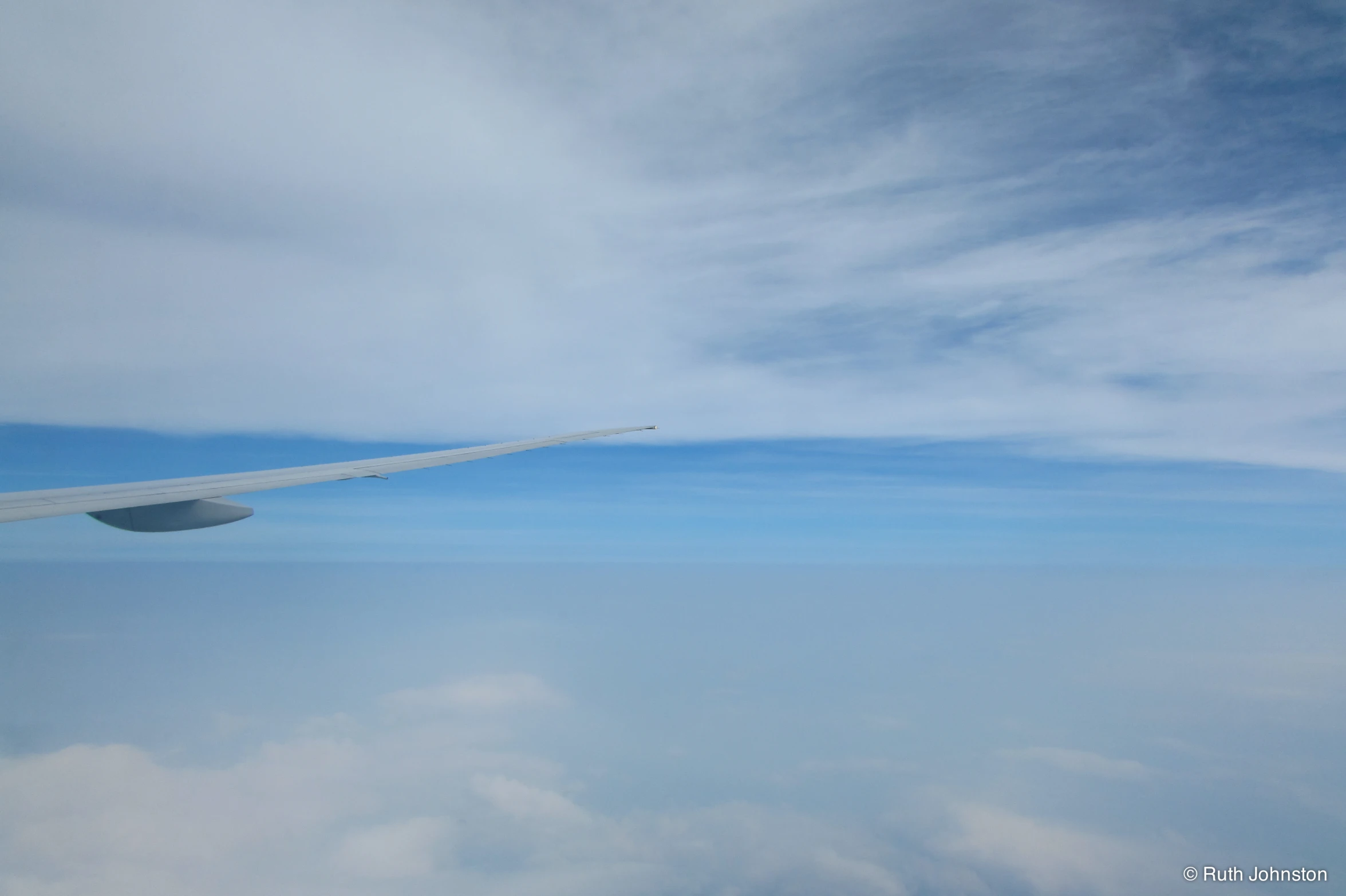 an airplane wing flying through the air with clouds in the background