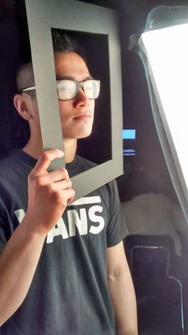 man with white glasses holding up mirror to look into window
