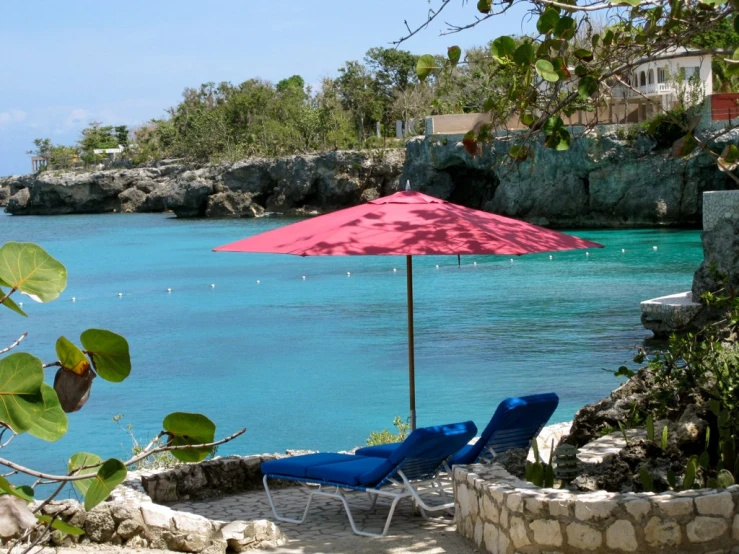 two beach chairs are near the ocean with an umbrella