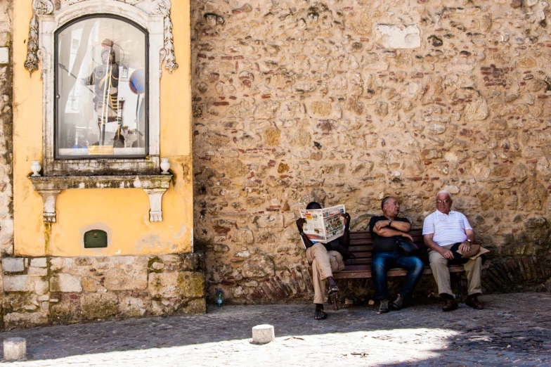 two people are sitting on a bench by a wall