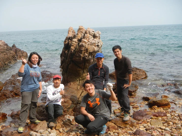 five people are standing around on rocks near the water