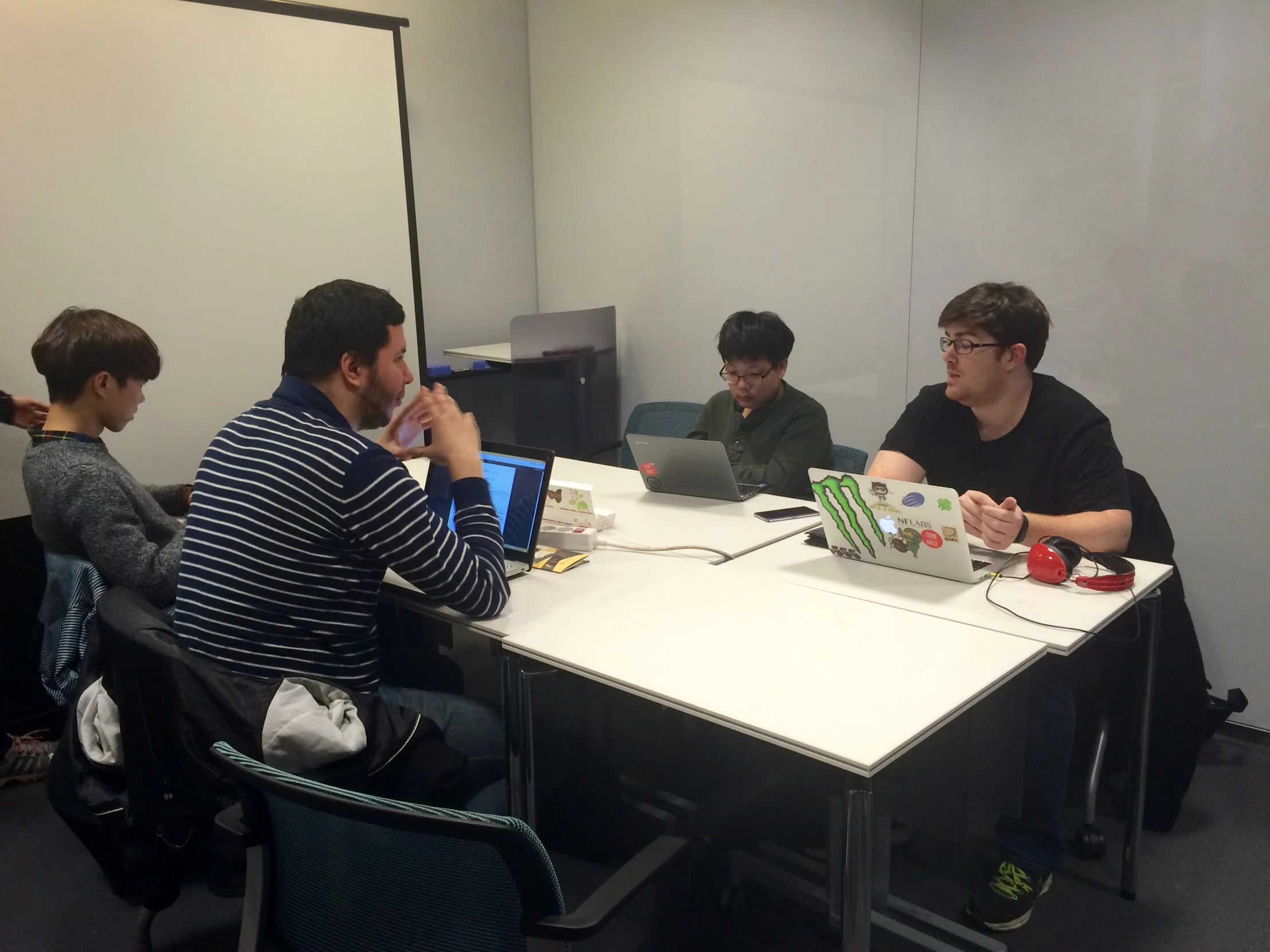 three men in an office, one sitting at a desk and two sitting in front of the same desk