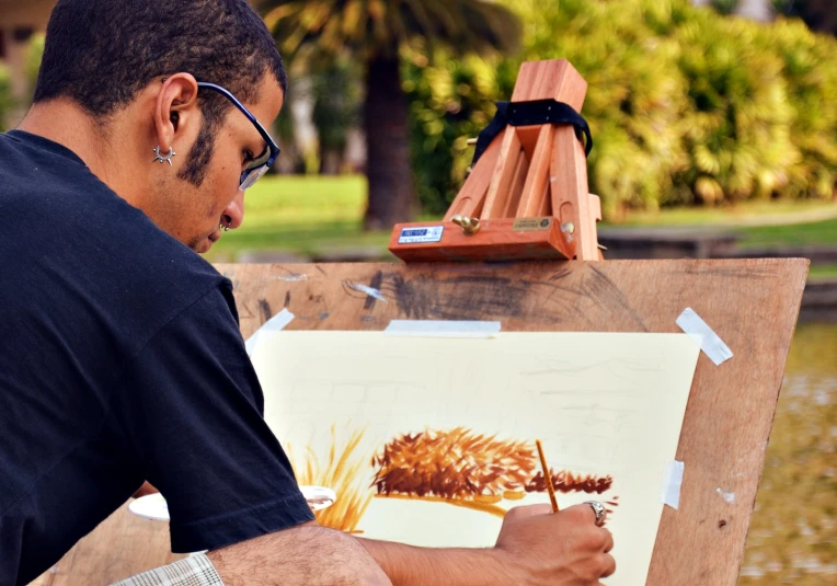 man is working on a painting while standing by a wooden easel