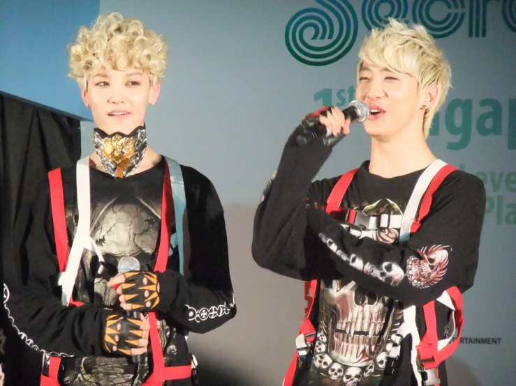 two boys with blonde hair and backpacks singing on stage