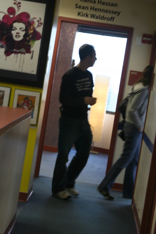 a man standing in a doorway next to another man walking