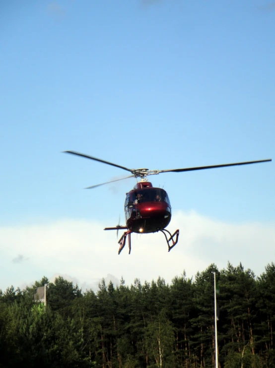 a red helicopter flying over a forest covered hillside