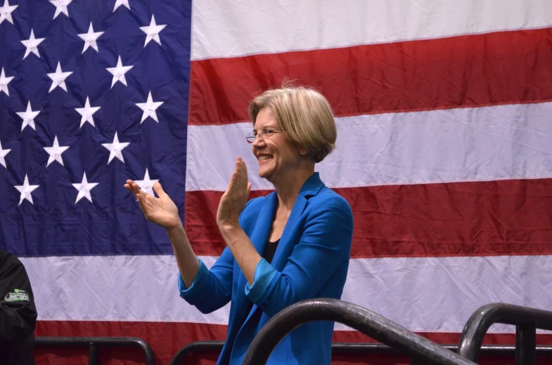 the woman smiles as she holds her hand up while standing next to a flag