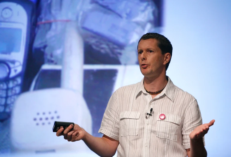 a man holding a cellphone while standing up with a screen in the background