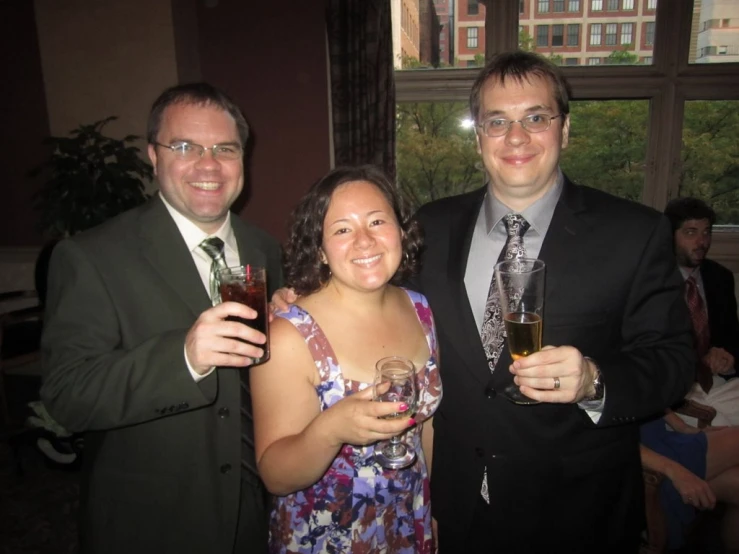 three people are smiling at the camera holding glasses