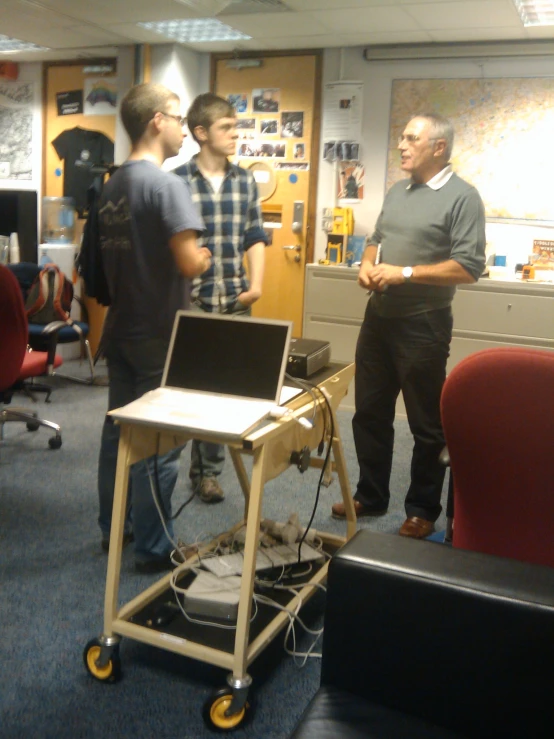 a group of men talking and looking at soing on a desk