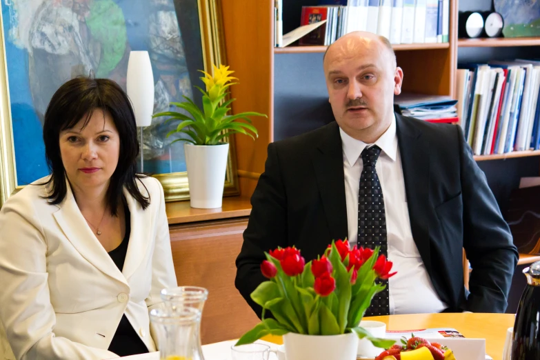 a couple sits at the table in front of a vase of flowers