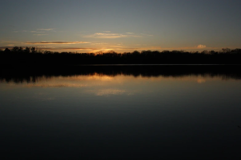 the sun is setting on the water next to a forest