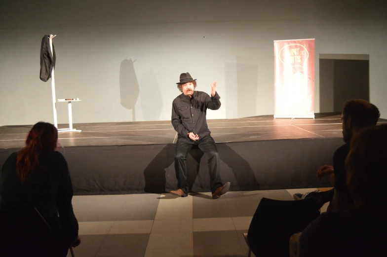 a man in black hat and shirt sitting on top of a stage