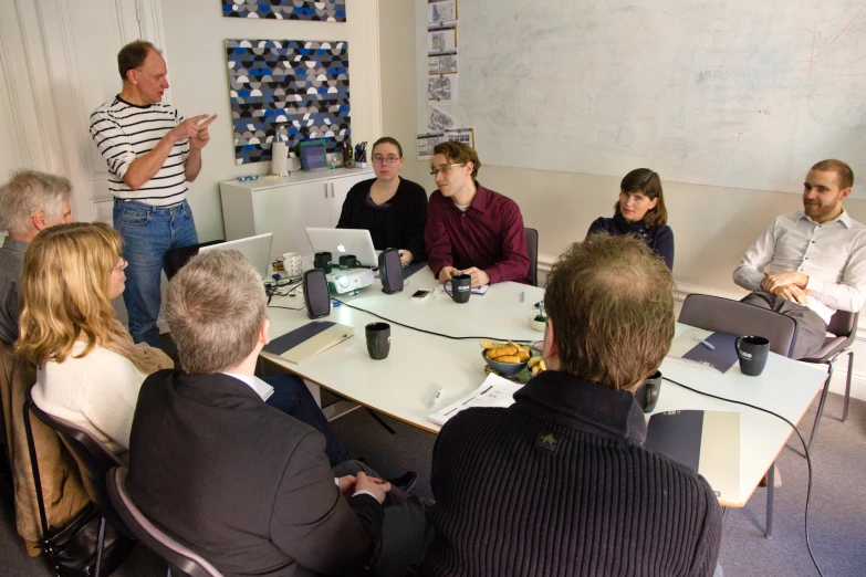 five men and two women in business attire gathered around a conference table talking