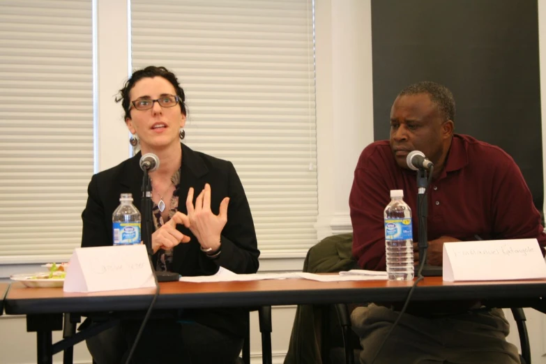 a woman sitting at a table speaking into microphones