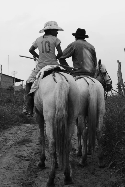 two men riding horses down a dirt road