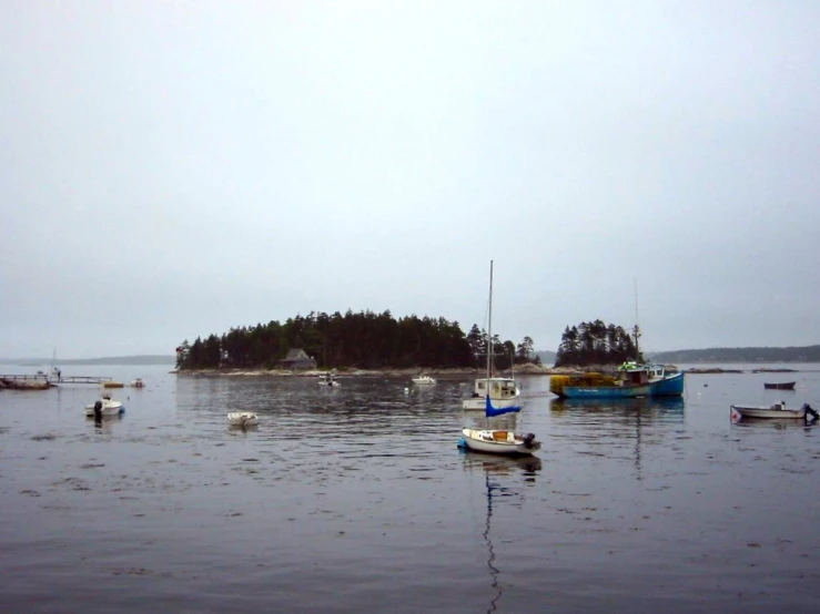 several small boats floating in the water on a cloudy day