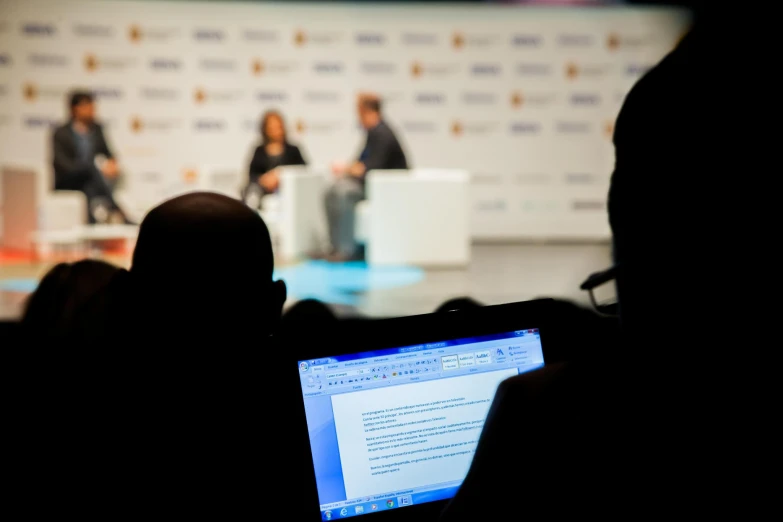 a person with a laptop at an event with people in the background