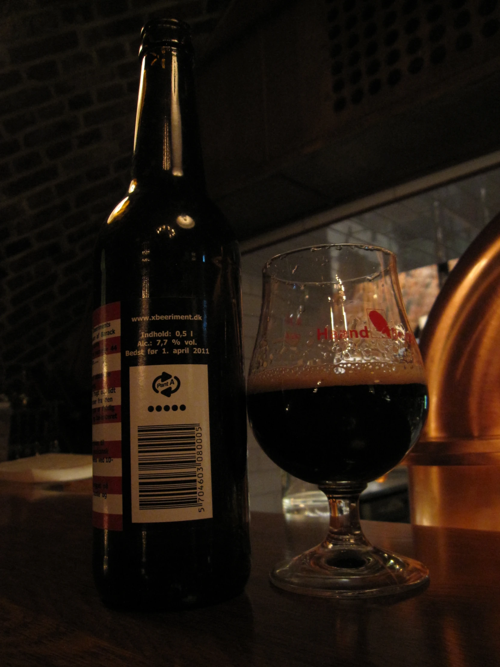 a bottle of beer on a wooden table and a glass of wine in front of it