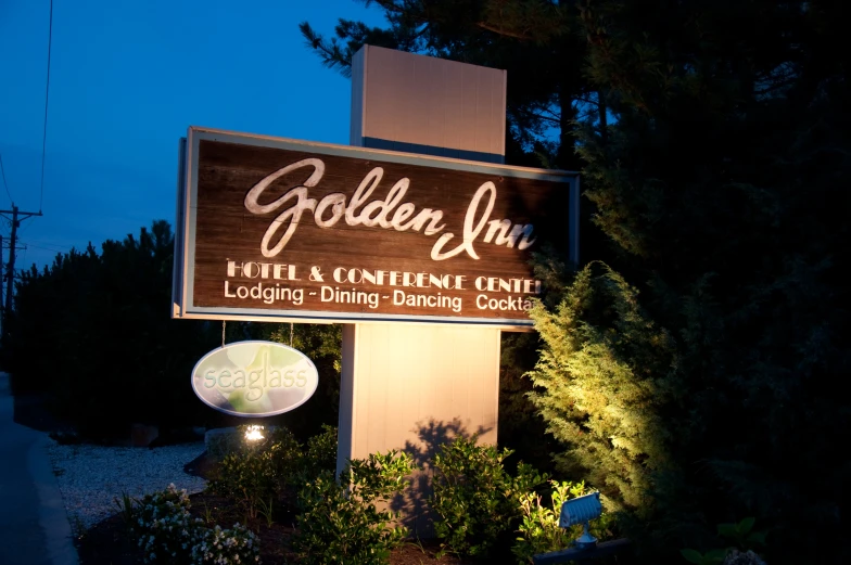 a lit up sign for a building with a tree and bushes behind it