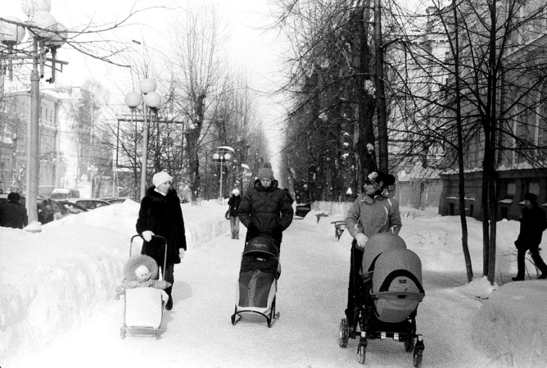 an old pograph of a snow covered street with people walking and hing their strollers