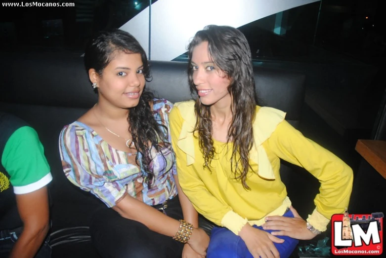 two woman sitting on a couch with a table behind them