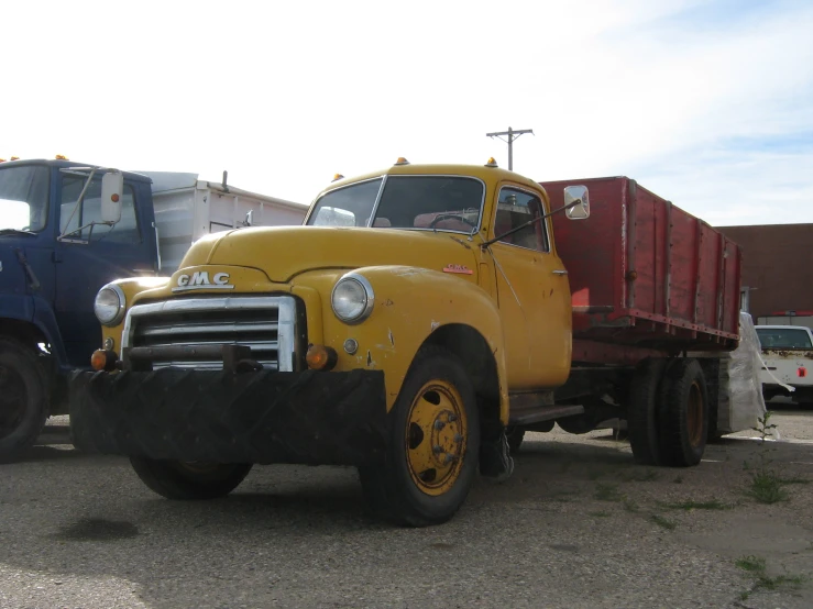 an old yellow truck sits parked by some large trucks