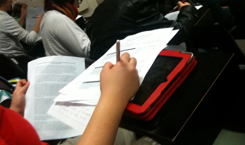 someone writing soing at the table while a woman sits at the back