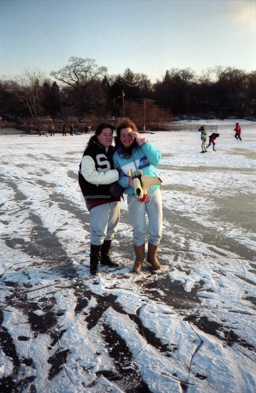 two women on ice rink next to trees and people