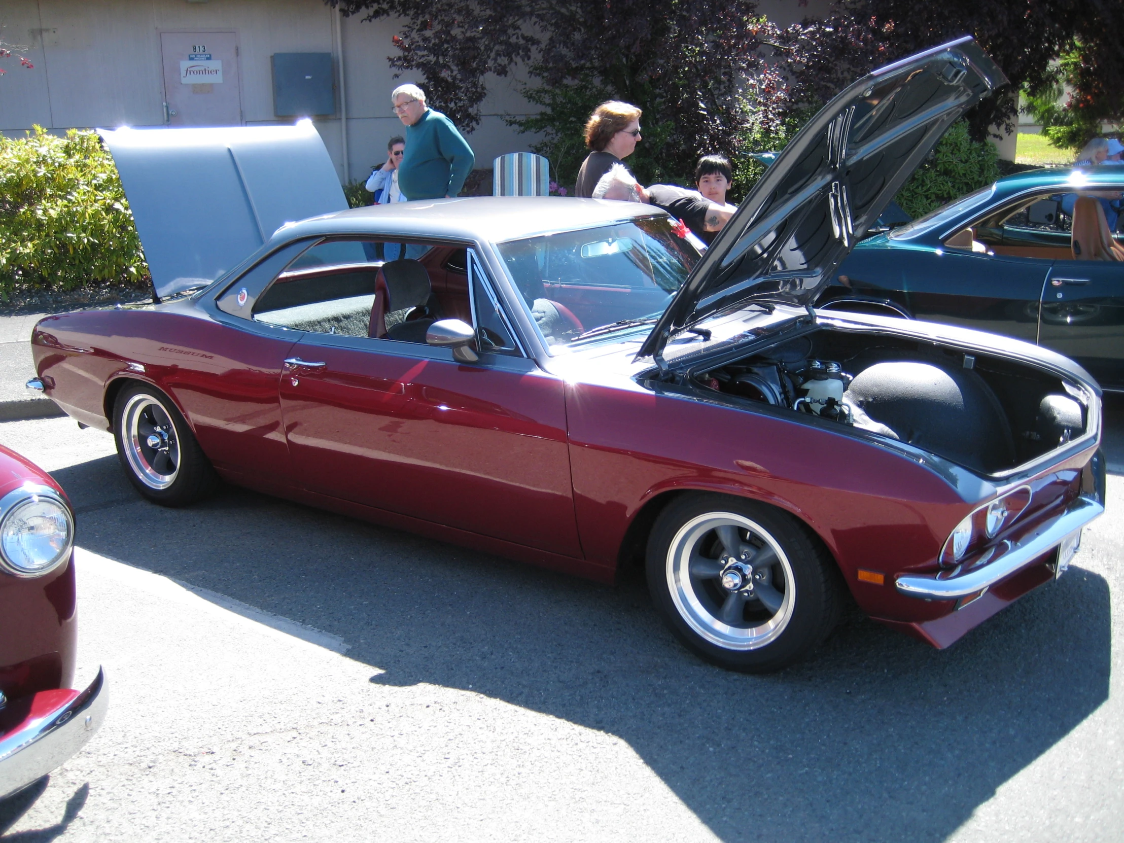 red muscle car with hood open parked in front of other cars