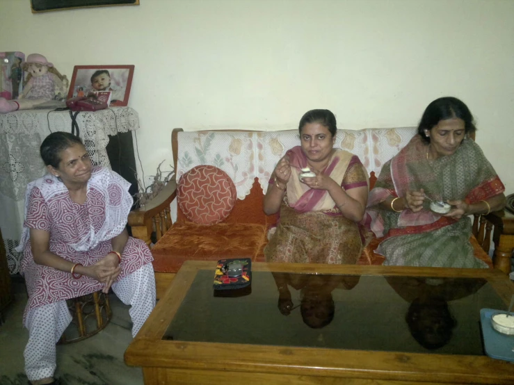 three women sit on sofas holding food, talking