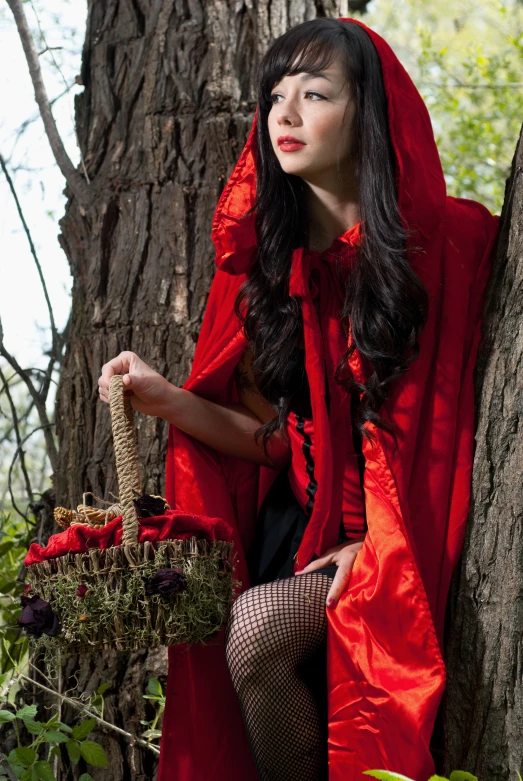 a young lady wearing red holding a basket in a forest