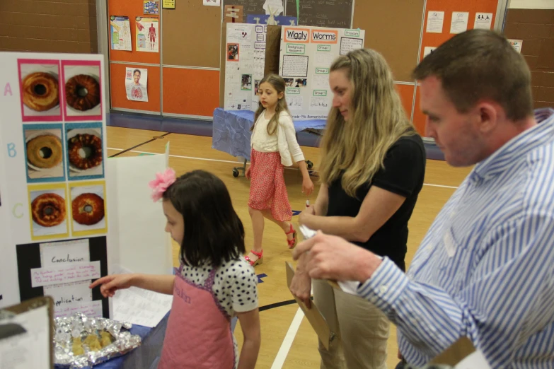 three children looking at a doughnut display in a school gymnasium