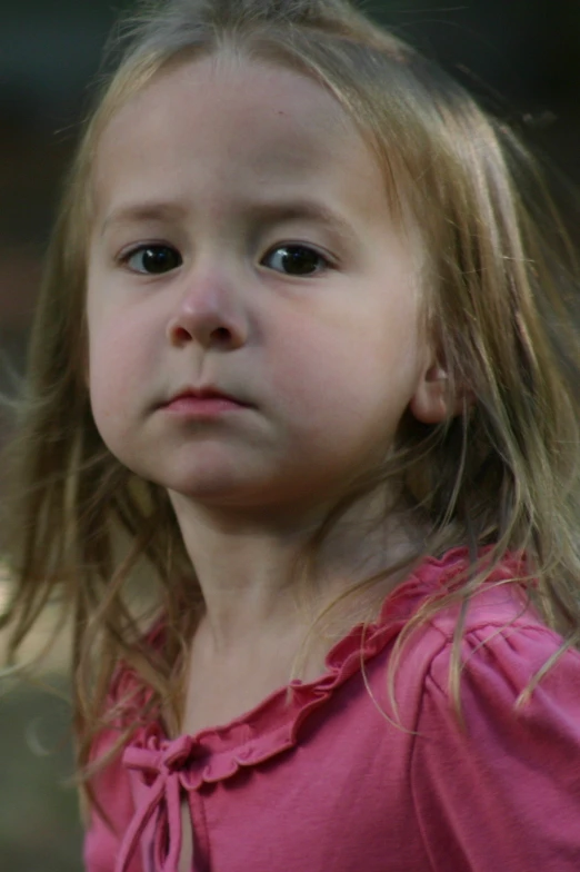 a little girl has long blonde hair wearing a red shirt